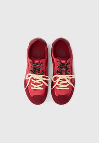 Κόκκινα αθλητικά παπούτσια από σουέτ και ύφασμα με μπεζ κορδόνια, διαθέσιμα με στρογγυλεμένη μύτη και σχέδιο σε μαύρα και λευκά κορδόνια, ενισχυμένη φτέρνα και σήμανση μάρκας.