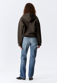 Übergroßer dunkelgrüner Hoodie mit Kapuze, kombiniert mit hellblauen geraden Jeans. Einfaches Design ohne sichtbare Muster oder Hardware-Details.