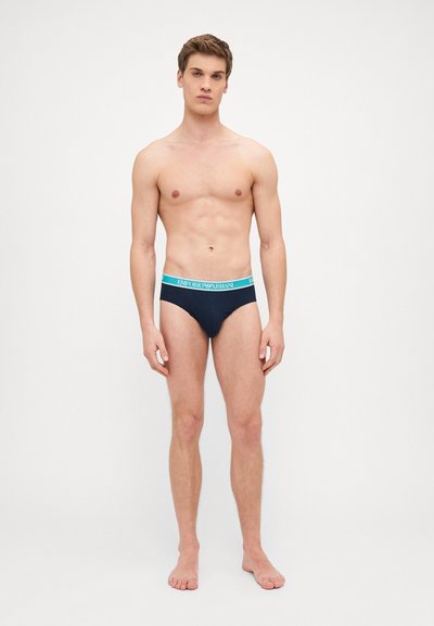 Slip da uomo blu navy con una vita elastica turchese in contrasto che presenta il logo "EMPORIO ARMANI", realizzati in un tessuto morbido e elasticizzato.
