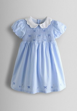 Gaiši zila kleita ar baltu Pītera Pāna apkakli, smockētu augšdaļu, pūkainām piedurknēm un izšūtiem loku rotājumiem apakšmalā. Izgatavota no mīkstas kokvilnas auduma.