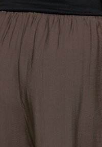 Top noir associé à une jupe marron taille haute et ample, avec un tissu froncé à la taille.