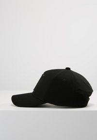 Casquette de baseball noire en tissu, avec une visière incurvée, des détails cousus et des trous de ventilation sur le dessus.