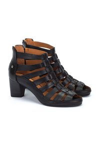 Sandalias de tacón alto de cuero negro con punta abierta, que presentan un diseño de tiras entrecruzadas, un acabado texturizado y un tacón bajo moderado.