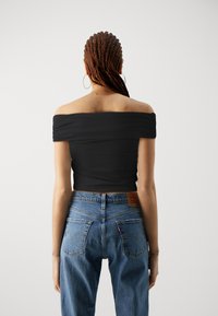 Svart off-shoulder crop top med tettsittende design, parret med lyseblå høytlivs denimjeans med fremtredende baklommer og søm.