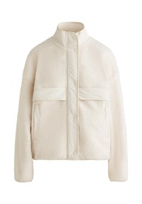 Kremno barvana flis jakna z visokim ovratnikom, pritisnimi gumbi in vodoravno pasico čez prsa. Ima dve sprednji žep.