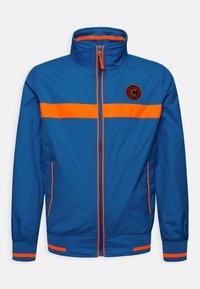 Modrá lehká bunda s oranžovými akcenty, zipovým uzávěrem, vysokým límcem a elastickými manžetami. Obsahuje logo na levé části hrudi a horizontální pruhy.