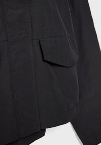 Čierna textilná bunda s vreckom so zapínaním na patent a čistými líniami. Materiál je hladký s matným povrchom, navrhnutý pre moderný vzhľad.