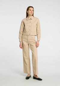 Ensemble en velours côtelé beige composé d'une veste courte et d'un pantalon, avec un col classique et un pantalon droit. Le tissu présente une texture rayée verticale.