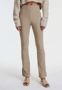 Beige, hoge taillebroek met zijsplitten aan de zoom, gemaakt van een soepele, rekbare stof, gecombineerd met lichtbeige open-toe hakken.