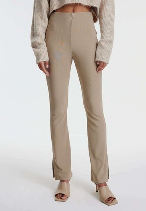 Beige, hoge taillebroek met zijsplitten aan de zoom, gemaakt van een soepele, rekbare stof, gecombineerd met lichtbeige open-toe hakken.