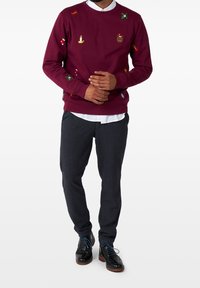 Burgundy sweatshirt med broderade julmotiv, kombinerad med textures mörka byxor och svarta skor med blå snören.