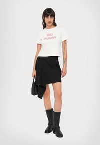 Valge lühendatud t-särk roosade pehmete tähtedega "SKI BUNNY", musta mähisega seelikuga ja põlvepikkuste mustade saapadega. Must käekott lõpetuseks.