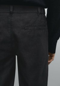 Dark gray pants made of textured fabric, featuring a back pocket and belt loops, shown from the waist down against a neutral background.
