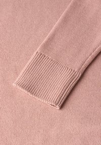 Détail d'un pull en tricot rose tendre avec une texture de poignet côtelé, des bords propres et un corps lisse avec une légère élasticité.