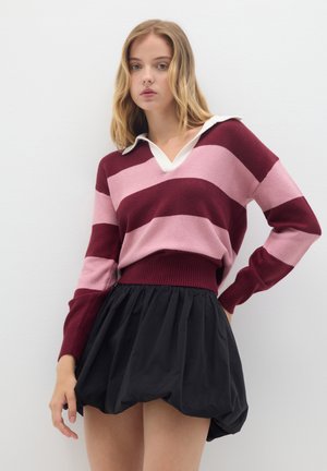 Striped sweater in burgundy and pink, featuring a V-neck and white collar. Paired with a black, voluminous skirt. Smooth fabric texture.