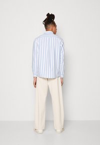 Camisa a rayas azul claro y blanca con cuello clásico, puños abotonados y un corte relajado, combinada con pantalones de pierna ancha color crema y zapatillas blancas.