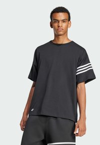 Melna oversized t-shirta ar īsām piedurknēm, ar trim baltām svītrām uz kreisās piedurknes un mazu logo uz priekšējā apakšmalas.