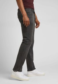 Jeans in denim grigio scuro con una vestibilità slim, caratterizzati da un classico stile a cinque tasche e una superficie leggermente testurizzata. Abbinati a sneakers bianche.