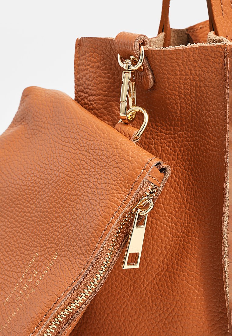 Braune Lederhandtasche mit strukturierter Oberfläche, ausgestattet mit einem abnehmbaren Beutel und goldfarbenen Hardware-Details. Sichtbares Reißverschlussdetail.