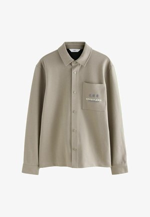 Beige skjorte med knapper lavet af blødt stof. Har en brystlomme med broderet tekst og et klassisk kravedesign.
