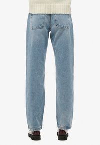 Vaqueros de mezclilla de color azul claro con corte recto, que cuentan con dos bolsillos traseros, dobladillos deshilachados y textura desgastada. Combinados con zapatos de plataforma negros.