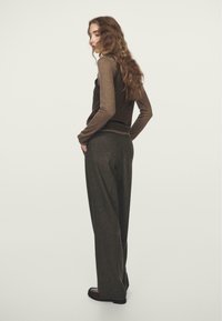 Brown long-sleeve top and dark gray wide-leg trousers. The top features a contrasting chest pocket; trousers have a smooth texture.