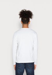 Langærmet hvid T-shirt lavet af bomuld, med rund hals og en afslappet pasform, parret med mørkeblå jeans. Minimalistisk design.