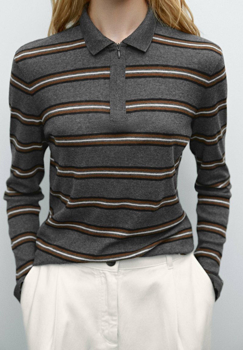 Polo shirt rayé gris avec un col zippé, présentant de fines rayures marron et blanches, associé à un pantalon de couleur claire. Texture lisse.