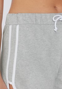Shorts en coton gris avec une taille à cordon de serrage, présentant des bandes blanches sur les côtés et une texture douce, conçus pour le confort et la mobilité.