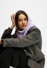 Sciarpa lavorata a maglia viola appoggiata su un blazer grigio strutturato, con una finitura testurizzata. L'outfit è abbinato a pantaloni neri, presentando un look stratificato.