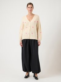 Κρεμ ζακέτα με V-λαιμόκοψη, ροζ κέντημα φοίνικα και κουμπιά. Συνδυασμένη με μαύρο παντελόνι φαρδιά πόδια και μαύρες γόβες.