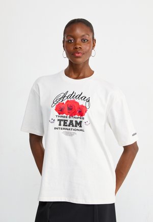 White cotton T-shirt featuring a graphic design with red roses and black text: "Adidas THREE STRIPES TEAM INTERNATIONAL" on the front.