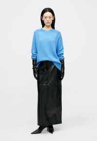 Világoskék kötött pulóver bordázott szegélyekkel, fekete bőr magas derekú szoknyával, fekete bőrkesztyűvel és hegyes fekete magassarkúval párosítva.