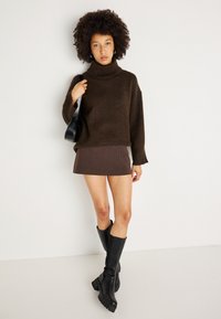 Burgundu adīts augstais apkakles džemperis ar ribotu apkakli, apvienots ar tumši brūnu svītrainu mini svārku un melniem augstiem zābakiem ar masīlu papēdi.