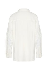 Weißes Leinenhemd mit langen Ärmeln, mit Spitzenverzierungen an den Ärmeln, Kragen und Knopfmanschetten. Glatte Textur und neutrale Farbe.