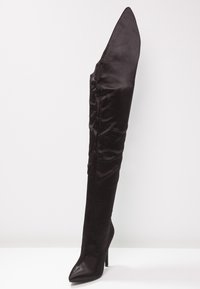 Zwarte stof over-de-knie laars met een spitse neus en een stilettohak. Beschikt over een gestructureerd oppervlak en een uniek, hoog, hoekig ontwerp.