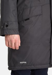 Parka grigia isolata con zip sul davanti, polsini a bottoni a pressione, tasche frontali e un logo sull'orlo. Texture liscia, design fino al ginocchio.
