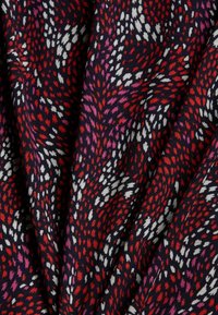 Flerfärgad tyg med en mörk marin bakgrund och spridda mönster i röd, rosa och vit, som skapar en texturerad visuell effekt.