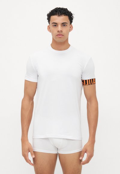 Camiseta blanca de manga corta con cuello redondo y un detalle de banda a rayas negra y naranja en la manga izquierda. Textura suave.