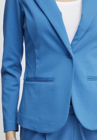 Blå kavaj med notched lapel, enkel knäppning och två framfickor. Tyg med en slät textur och skräddarsydd passform.