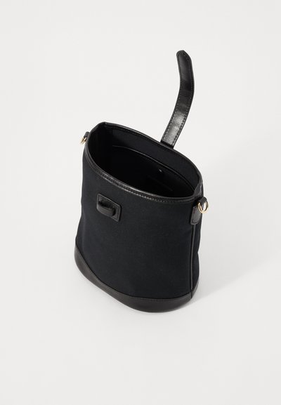 Svart kanvasveske med en glatt lærbase og pynt. Har et håndtak på toppen og et innvendig rom, minimalistisk design og ingen synlige mønstre.