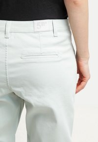 Světle mátově zelené kalhoty vyrobené z měkké tkaniny, s hladkým povrchem, zadní kapsou a značkovou etiketou na pase.