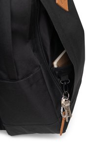 Mochila negra con un bolsillo con cremallera donde se pueden ver un cuaderno y llaves. El exterior tiene una textura suave con un acento de cuero.