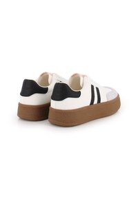 Zapatillas blancas con acentos negros, suela marrón texturizada y tres rayas negras. Presentan una puntera de ante y un detalle rosa claro en el cuello.
