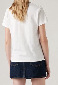 Weißes Baumwoll-T-Shirt mit kurzen Ärmeln, kombiniert mit einem dunklen Jeans-Minirock, der Taschen und kontrastierende Nähte aufweist.