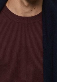 Pull en maille côtelée bordeaux avec un col rond, associé à un cardigan bleu foncé, présentant une texture douce et un design superposé.