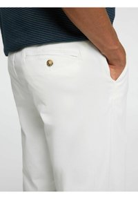 Witte broek met een gladde textuur, voorzien van een achterzak en een knopdetail in goudtint. Draag met een donker gestreept shirt.