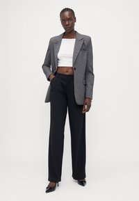 Grå rutete blazer med spisse lapel, svarte vide bukser og en hvit crop top. Tilbehøret inkluderer hoops-øreringer og svarte hæler.