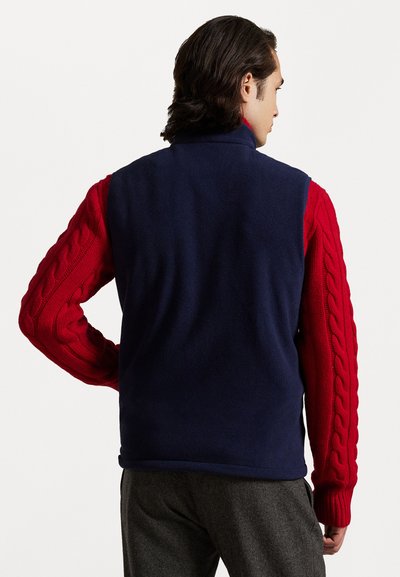 Chaleco de forro polar azul marino con mangas de punto en color rojo, que presenta un cuello alto y un diseño ajustado. Los acentos texturizados realzan la apariencia general.