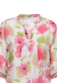 Camicia a maniche corte con bottoni, decorata da fiori rosa e verdi su sfondo bianco, con due tasche anteriori e un tessuto morbido e leggero.